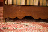 Scalloped wooden base and leg of an antique settle chair, showing plaid upholstery and patina.