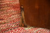 Antique settle chair wooden leg showing bottom discoloration and wear on a red braided rug.