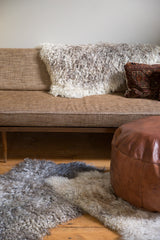 Soft angora throw rug with shaggy grey and white wool, next to a leather pouf.