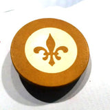Round brown decorative object with ivory circle and dark brown fleur-de-lis.