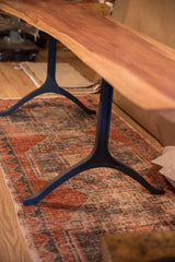 Sleek, three-pronged hand-forged iron legs supporting the warm-toned live edge redwood top.