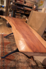 Detailed view of the live edge redwood table's smooth finish and hand-forged iron leg.