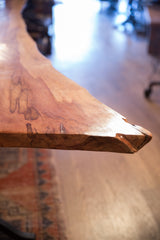 Sculpted live edge corner of a redwood table showing warm, figured wood grain.