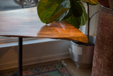 Corner detail of the live edge redwood table showing the warm finish and hand-forged iron leg.