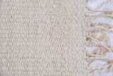 Handmade blanched jute rug texture with dense weave and natural braided fringe.