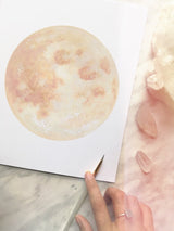 Blush Moon Art Print corner with blush pink watercolor, a hand with ring, and paintbrush.