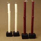 Matte black cast iron candle holders with textured dark red and creamy white tapers.
