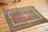 Antique Kazak rug corner displaying geometric reciprocating border, red field, and tattered fringe.