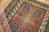 Antique Kazak rug detail: madder red field with blue geometric motif, reciprocating border, showing wear.