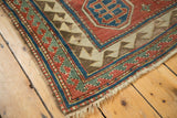 Antique Kazak rug corner with madder red reciprocating borders, tattered fringe, visible foundation.