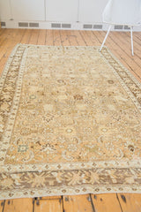 A vintage Malayer carpet with a distressed, neutral palette laid out on a wood floor.