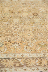 Soft, worn texture of a distressed Malayer carpet in warm sand, gold, and bronze tones.