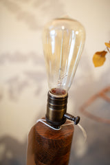 Close-up of the vintage Edison bulb and brass socket on the lamp's round oak base.