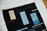 Abstract hand-woven pattern featuring blue, black, beige blocks, and thin red lines.