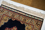 Corner view of a vintage Hereke rug showing the woven signature on its kilim skirt and ivory fringe.