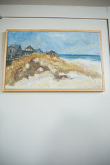 Grace B. Keogh 'Houses on Beach' painting framed in light wood on a white wall.