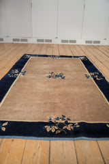 Beige open field of the Peking rug with navy border and blossoming blue motifs.