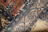 Vintage Malayer rug, folded to show woven foundation, rust pile, and black-wrapped edge.