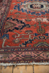Detail of vintage Malayer rug's brick red field, geometric vinery, noticeable wear, and tattered fringe.