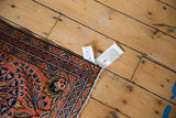 Dargezine rug corner, dusty brick red field, navy border, serrated floral motifs, white fringe.