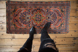 Persian Dargezine runner corner, displaying dusty brick red field, navy border, and budded floral vines.