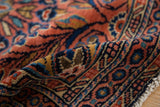 Close-up of vintage Dargezine rug pile, showing dusty brick red, navy floral details and fringe.