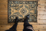 A distressed vintage Lilihan rug mat shown for scale on a rustic floor.