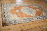 Distressed Kerman rug corner with navy blue border, sandalwood field, and ornate Rococo spandrel.