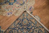Vintage distressed Kerman rug corner folds, exposing worn pile with pink, blue rococo details and tight border weave.