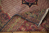 Vintage Khorassan rug's curled corner: red boteh field, navy and gold traditional border, ivory fringe.
