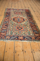 Hand-knotted vintage Heriz rug close-up showing geometric motifs, serrated leaf border, and tattered fringe.