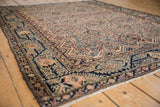 Angled view of a vintage Malayer rug highlighting the serrated floral designs and navy blue vine border.