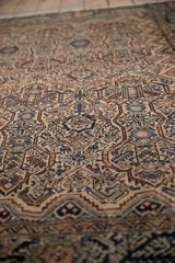 Angled view of a vintage Malayer rug showing the low-pile texture and detailed serrated floral panels.
