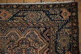 Corner of a vintage Malayer rug with a detailed navy vine border and ivory fringe.