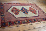 Angled perspective on an antique Afshar rug showing its stepped triple medallions and floral borders.