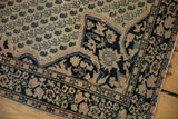 Antique Farahan Sarouk rug corner: ivory field, blush floral spandrel, dark navy border, bare selvage.