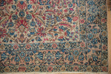 Vintage Kerman rug corner showcasing ivory millefleur field, dusty rose border with blue florals.