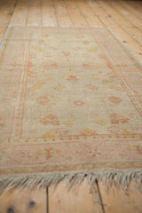 Vintage Oushak rug viewed from an angle, highlighting its low pile and dusty rose border.