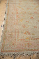Pinwheel floral main border in dusty rose and saffron on a low-pile vintage Oushak rug.