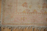 Hand-knotted corner of a vintage Oushak rug showing the floral border and short ivory fringe.