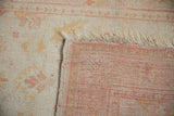 Corner of a vintage Oushak rug folded back, showing the hand-knotted weave and ivory pile.