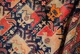 Rolled antique Karabagh rug: geometric navy, red, orange patterns, with visible pile wear.