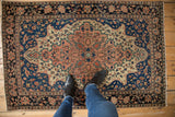 Antique Farahan Sarouk rug's scalloped medallion and intricate floral vinery in blush, ivory, and indigo.