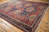 Textured antique Soumac carpet detail: cherry red field, navy blue medallion, pinwheel florals, geometric border.