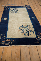 Corner of a vintage Peking rug showing cobalt blue border and tree with bird motif.