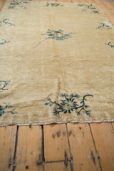 Lower edge of antique Peking rug, showing blue floral branch on an aged cream field.