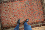 Brick red field of Vintage Malayer rug, staggered boteh motif, sky blue, blush, charcoal, visible foundation, tattered edge.