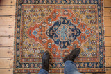 Vintage Heriz rug shown for scale, displaying a geometric medallion in brick red, deep gold, and navy blue.