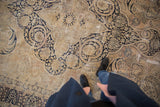 Distressed Kerman carpet: antique ivory field, dark navy scrolling vinery, and visible low pile wear.