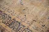 Distressed vintage Kerman carpet's textured pile with dark navy vinery on worn ivory.